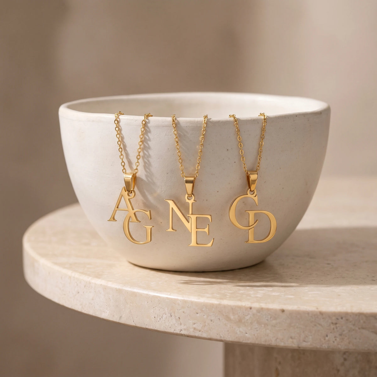Collier double lettre posé dans une coupelle, finition dorée