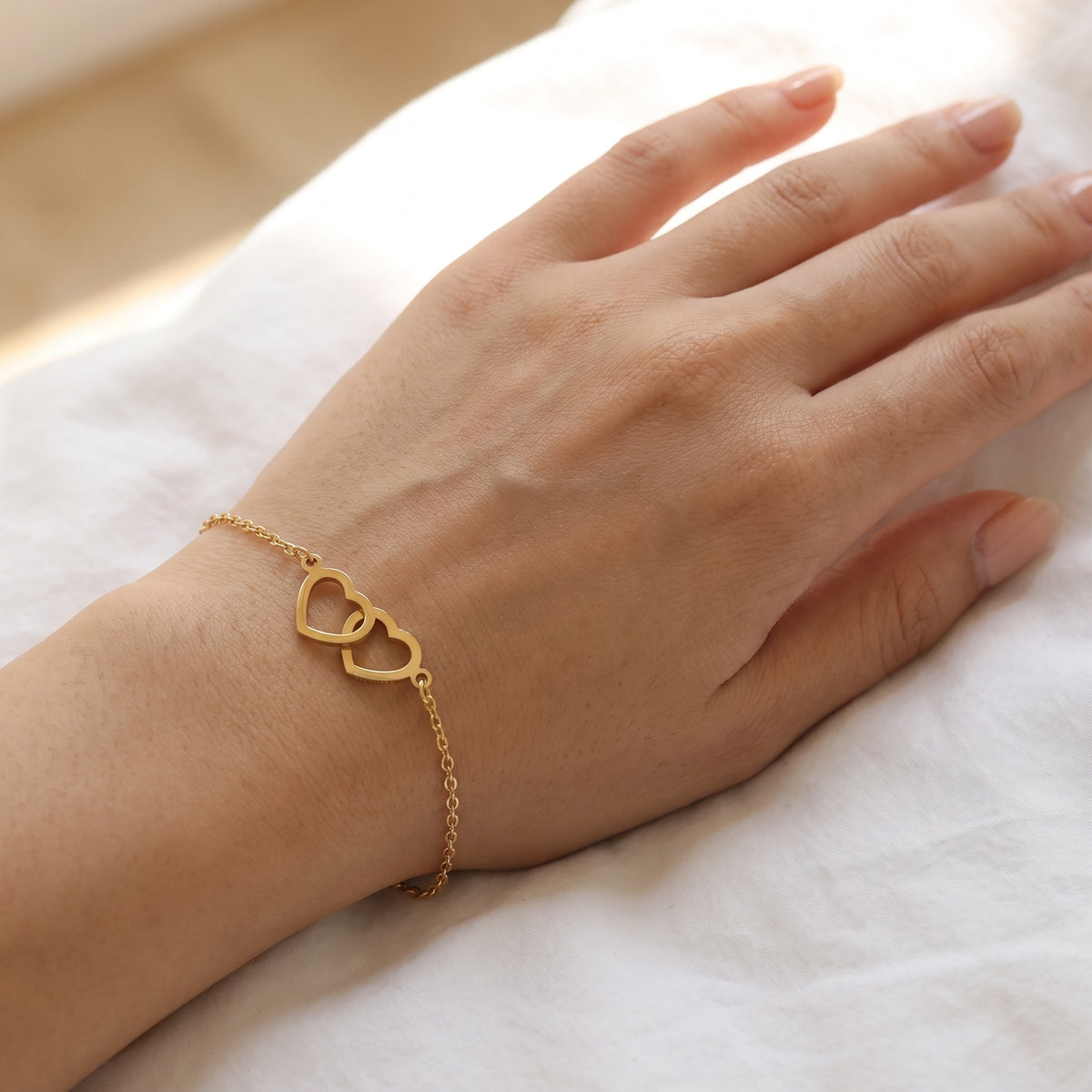 Bracelet personnalisé assorti en or porté au poignet, deux cœurs enchaînés
