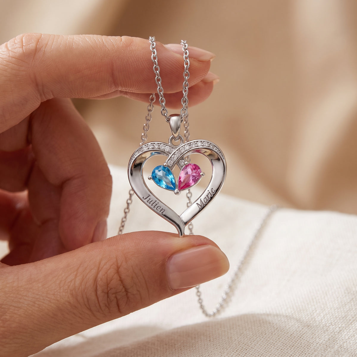 Pendentif cœur gravé de deux prénoms tenu entre les doigts