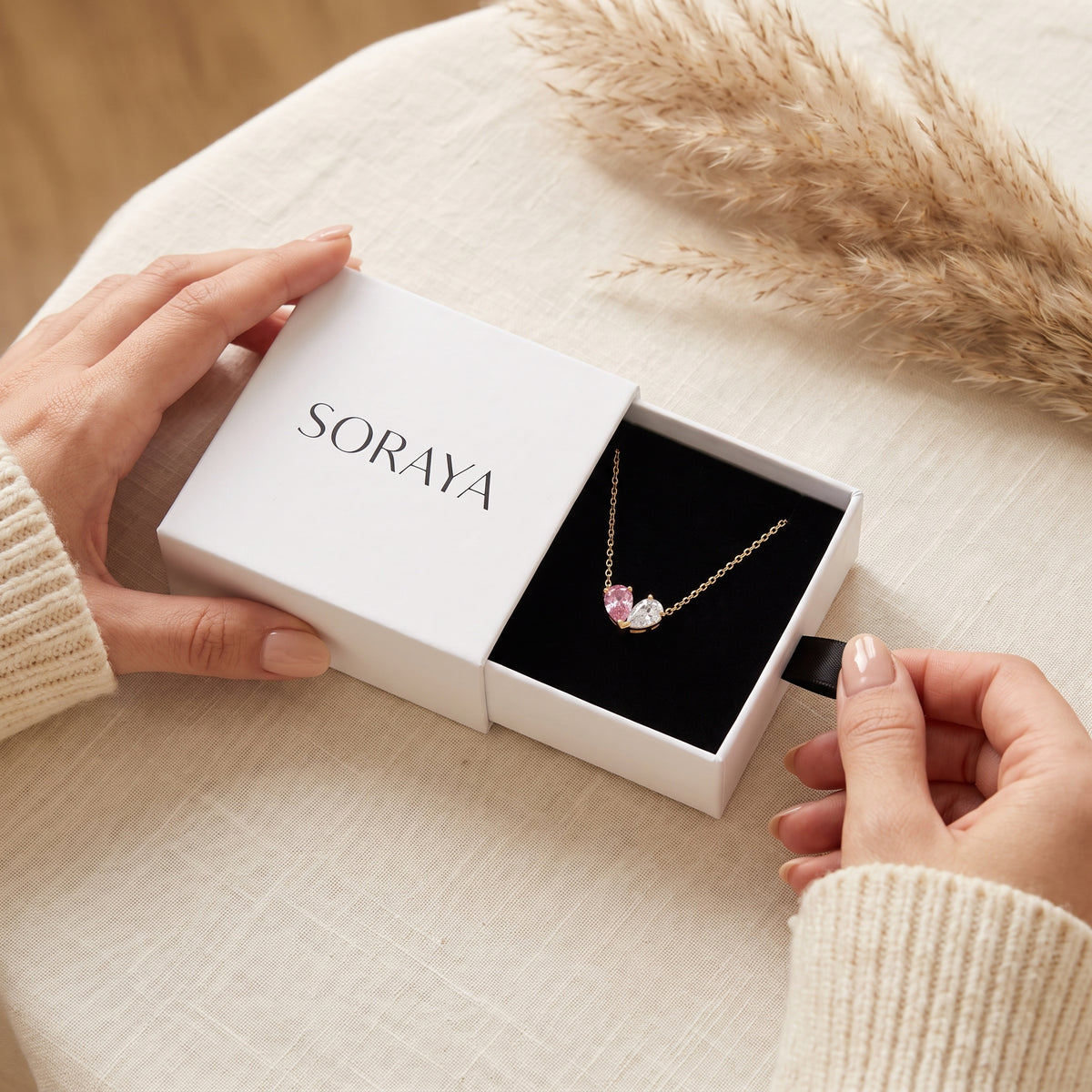 Mains ouvrant l'écrin SORAYA avec le collier Liora